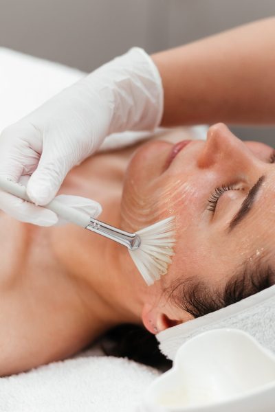 Cosmetology beauty procedures. Lady receiving rejuvenation anti aging treatment, facial chemical peel therapy in beauty salon or medical center. Wellness. Mask with retinol. Close-up, ads